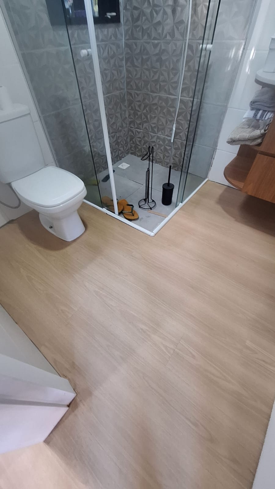 Banheiro com box de vidro e piso vinílico em tom claro