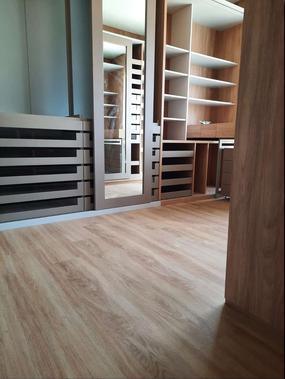 Closet planejado com piso vinílico em carvalho claro, gaveteiros, prateleiras e espelho de corpo inteiro
