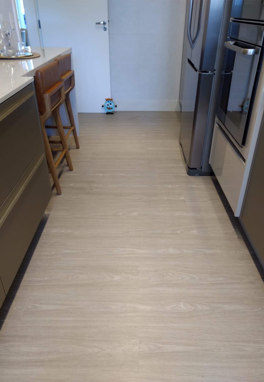 Cozinha com bancada branca, eletrodomésticos de inox e piso vinílico em tom claro