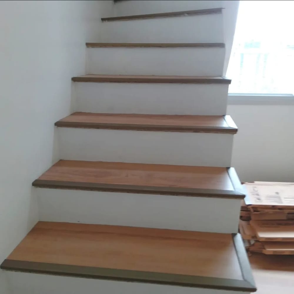 Escada com degraus revestidos em piso vinílico claro e janela ao fundo