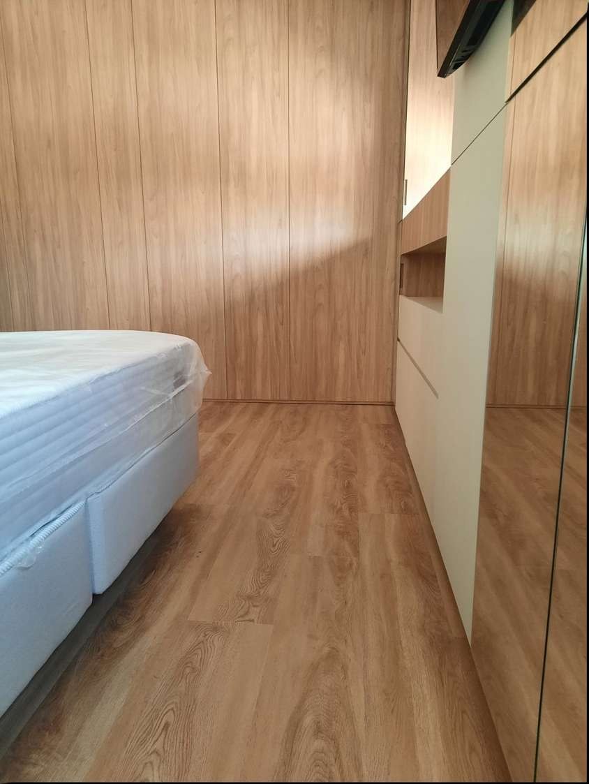 Dormitório com painel de madeira na parede, armário planejado e piso vinílico em carvalho claro