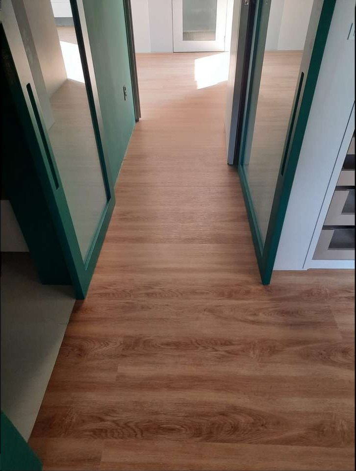 Hall de circulação com piso vinílico em carvalho, portas de vidro com moldura verde nas laterais