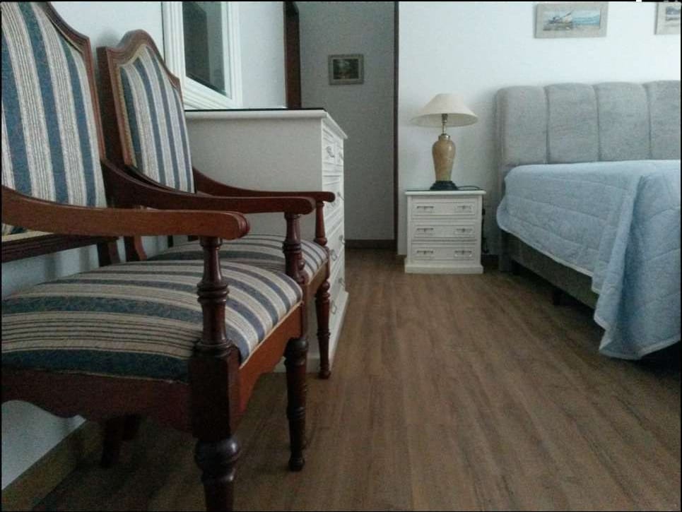 Quarto mobiliado com poltronas antigas, cama e piso vinílico em tom médio