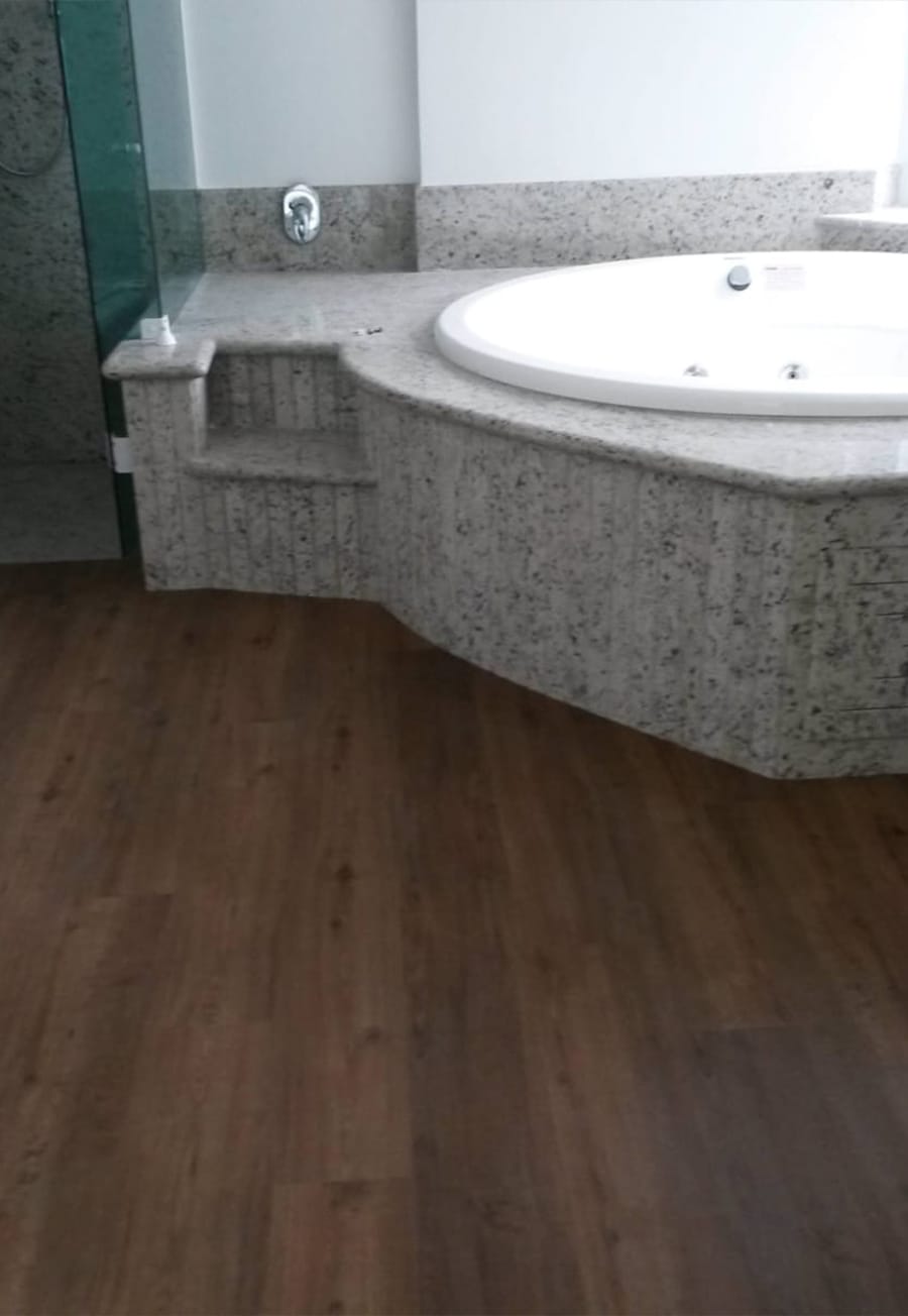 Piso vinílico escuro contornando banheira revestida de granito claro