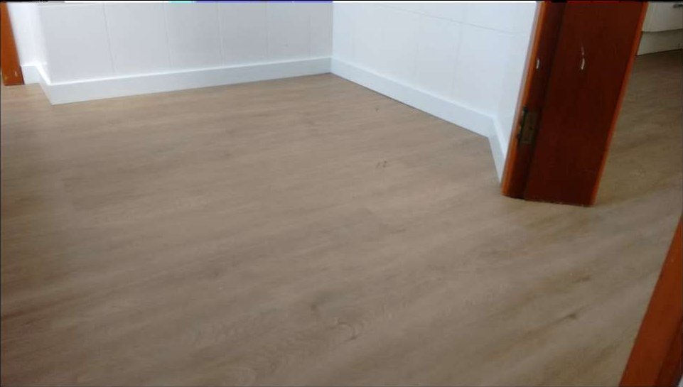 Ambiente com piso vinílico claro e rodapé branco acompanhando o recorte da parede até a porta