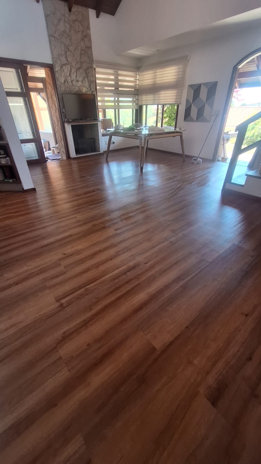 Sala de estar ampla com piso vinílico tom nogueira, lareira de pedra e janelas ao fundo