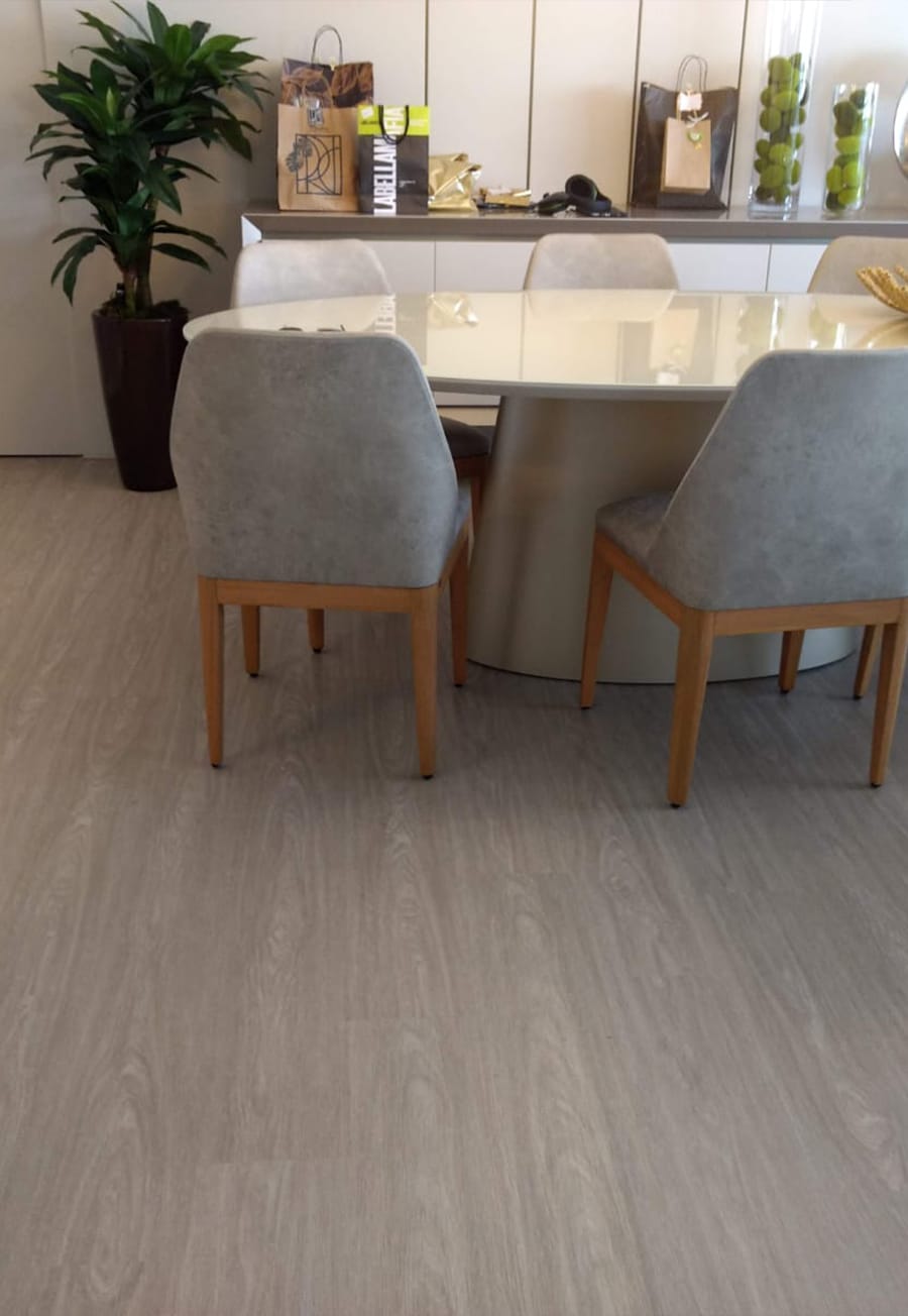 Sala de jantar mobiliada com mesa oval, cadeiras estofadas e piso vinílico cinza claro