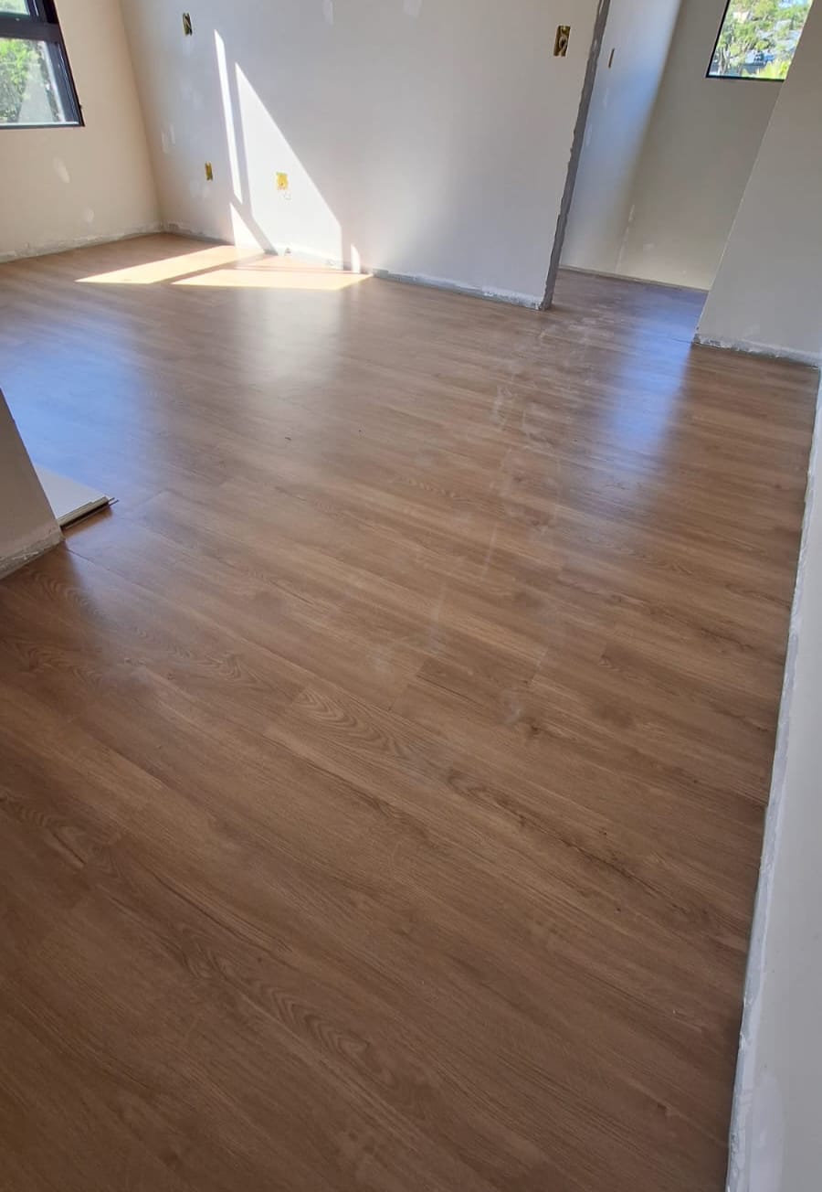 Sala vazia com sol entrando pelas janelas e piso vinílico em tom carvalho