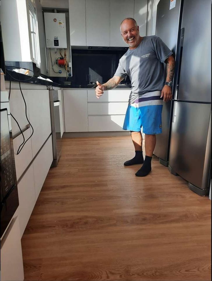 Sandro Marques em pé sobre o piso vinílico recém-instalado de uma cozinha, na entrega da obra